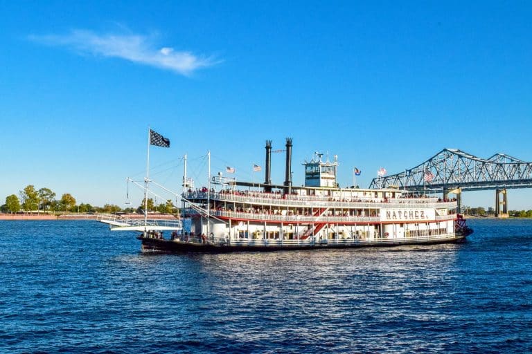 USA Reisen - Ein großes Mississippi-Flussschiff auf dem Wasser mit einer Brücke im Hintergrund.